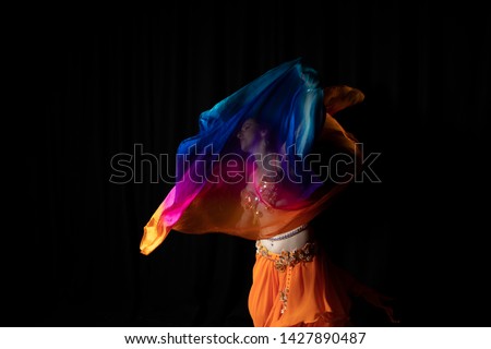 A colorful dancer spinning with multi color silk veil in her hands, creating  a beautiful, artistic frozen motion, portraying grace and energy of belly dancing.  Royalty-Free Stock Photo #1427890487