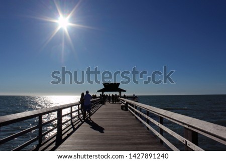 Visitors stand on landmark The Pier in Naples FL, popular for exquisite sunsets and boatless fishing, as blazing sun begins to set in the cloudless blue sky. Gulf of Mexico. 