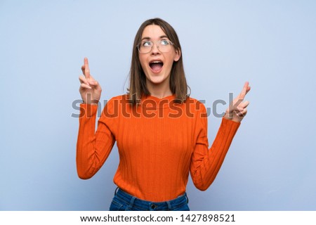 Teenager girl over blue wall with fingers crossing
