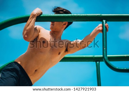 Handsome shirtless young man doing street workout on parallel bars