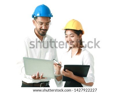 Two engineers wear safety helmets and discuss about work project with copy space isolated on white background. Man with mustaches hold laptop computer, smiling pretty Asian woman hold document file.