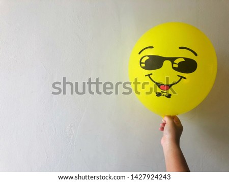 Hand hold a yellow balloon with smiley face on white wall background. Space for text