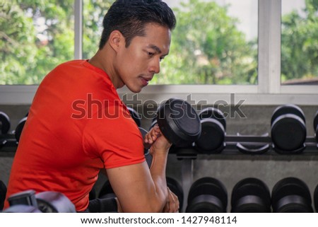 Asian male having exercise lifting dumbbell in gym