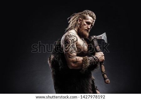 Medieval warrior berserk Viking with tattoo with axes attacks enemy. Concept historical photo Royalty-Free Stock Photo #1427978192