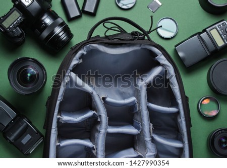 Equipment professional photographer on green background. Empty photo backpack, camera, lenses, flashes, light filters. Top view