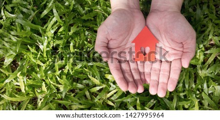 Green house concept. Close up hands holding white paper house on green glass background. Green environment protect the world eco energy earth day concept panoramic banner