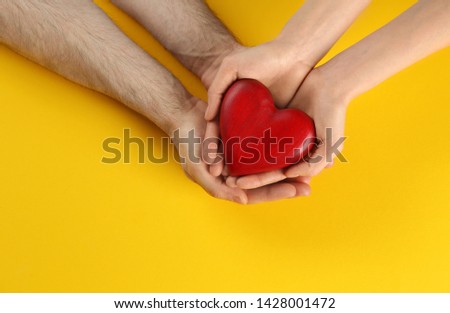 Couple holding decorative heart on color background, top view