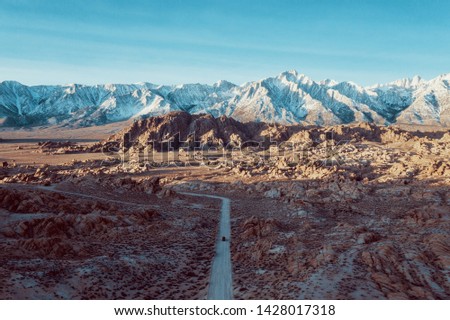 Alabama hills seen from above, with a dirty road. Mountains in the background. blue sky and desert view. 