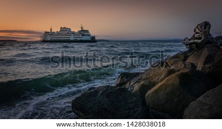 As the Mukilteo Ferry slips into the sunset the waves from Possession Sound break onto the boulders of the breakwater protecting the Mukilteo Lighthouse. Royalty-Free Stock Photo #1428038018
