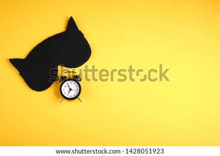 Black sleep mask with clock on yellow background composition, cat mask with ears, flat lay and top view photo