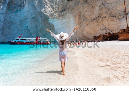 Happy tourist woman with white hat walks on the famous shipwreck beach, Navagio, on Zakynthos island, Ionian Sea, Greece