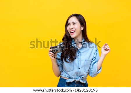 Attractive energetic Asian woman happily holding cemara isolated on yellow studio background