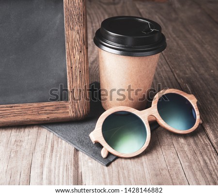 coffee paper cup with vintage slate chalk board, on grunge wood table, and sun glasses