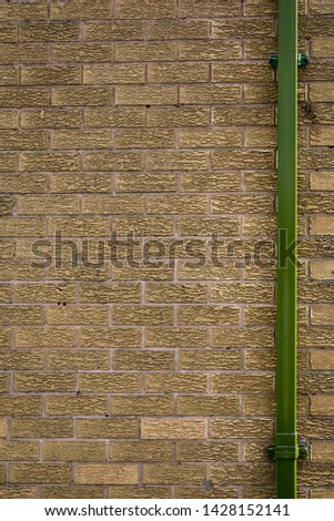 A bright green drainpipe set against the right-hand side of a brown brick wall. Image has copy space on top, bottom, and left-hand side.