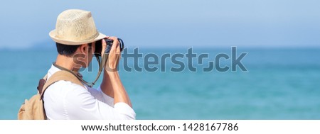 Candid of young attractive asian man hold camera taking photo in blue sky and sea view background. Happy asian hipster male photographer in youth freedom culture lifestyle travel in rear view concept.