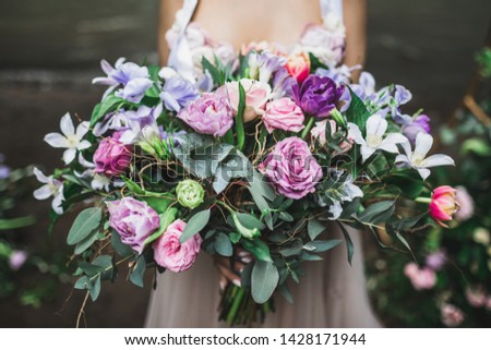 Bride holding b beautiful colorful wedding bouquet of roses, peonies and tulips in bright pink, coral and purple colors.