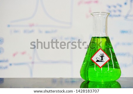 Erlenmeyer flask with Green liquid and chemical hazard warning symbols labels (hazardous to the environment sign) on whiteboard with chemical learning background.	

