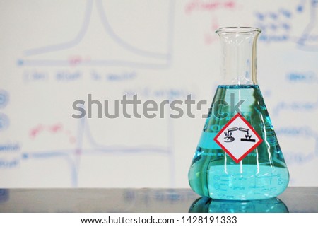 Erlenmeyer flask with Bright blue liquid and chemical hazard warning symbols labels (corrosive symbol) on whiteboard with chemical learning background.