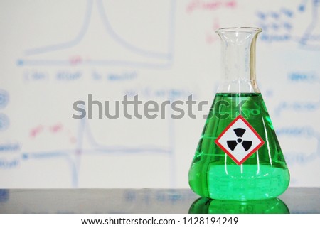 Erlenmeyer flask with Green liquid and chemical hazard warning symbols labels (radioactive sign) on whiteboard with chemical learning background.