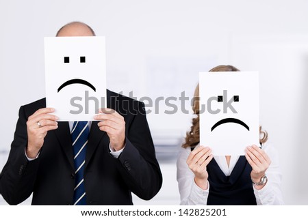 Businesspeople holding sad smileys on placard in front of faces at office