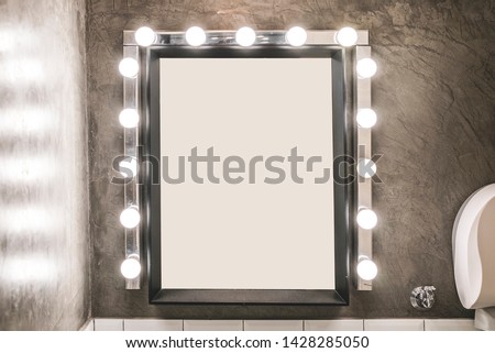 Blank makeup mirror with light bulbs on a concrete wall in a toilet