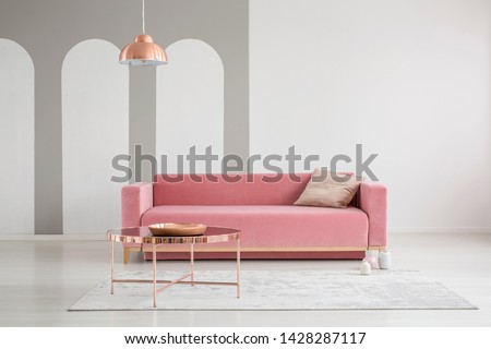 Patterned pillow on a velvet pink sofa and copper gold accessories in a feminine living room interior with empty white wall Royalty-Free Stock Photo #1428287117