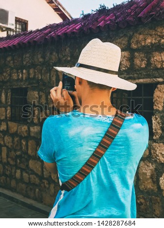 Summer vacation Mobile photography A young male tourist in a straw hat is taking a picture of an old street on his smartphone