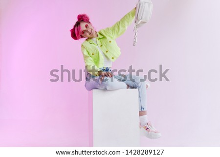 woman with a pink hair hairstyle sits on a cube in the hands of a white bag