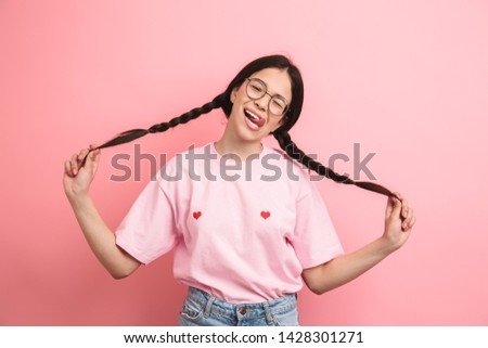 Portrait closeup of european happy girl with two pigtails wearing eyeglasses having fun and smiling at camera isolated over pink background