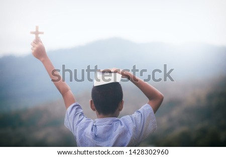 Boy christian holding cross and Bible in hand with mountain background. young christian concept.