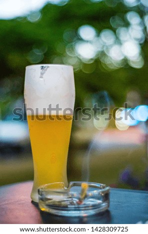 glass of beer on a wooden table with ashtray with smoke cigarette