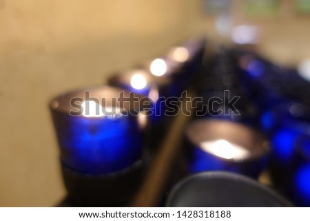 Blur picture of rows burning candles in blue transparent glass in the church. Christian normally lighting candle for memorialize of departed, honor special occasions, or symbolize the light of Christ.