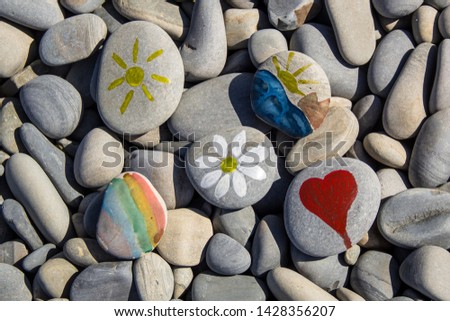 Bright sun painted on pebble. Pebbles and sea background in summer