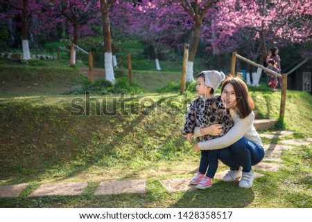 A beautiful Asian mother embraced her daughter in a park full of cherry blossoms.