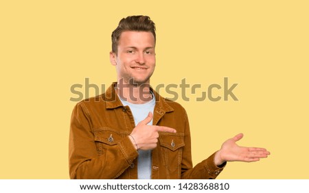 Blonde handsome man holding copyspace imaginary on the palm to insert an ad