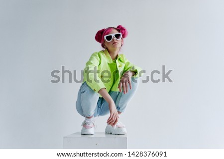 woman with pink hair and glasses sits on a cube