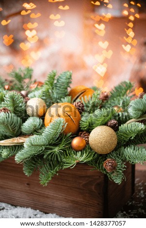 Christmas mood. Beautiful festive arrangement of fresh spruce in a rustic wooden box. Bokeh hearts of Garland lights on background. Decorated with slices orange, gold balls , cones