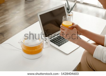 In the afternoon, Asian girls are holding a glass of freshly squeezed orange juice to work on a laptop.
