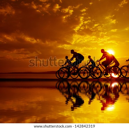 Image of sporty company friends on bicycles outdoors against sunset. Silhouette A lot phases of motion go of five 5 cyclist along shoreline coast Reflection sun on water Copy Space for inscription