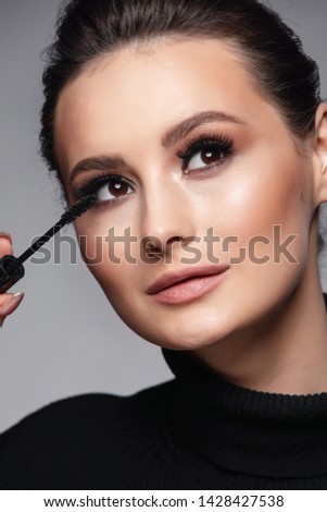 Beauty Cosmetics.Woman applying black mascara on eyelashes with makeup brush. photos of appealing brunette girl on gray background.High Resolution
