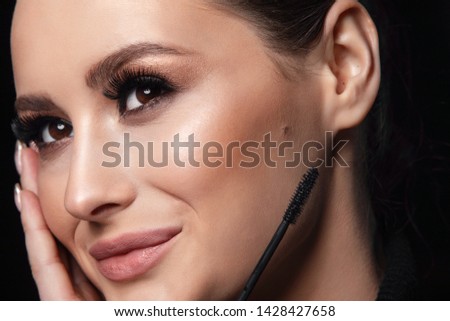 Beauty Cosmetics.Woman applying black mascara on eyelashes with makeup brush. photos of appealing brunette girl on black background.High Resolution
