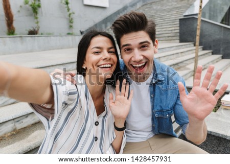 Image of happy young amazing loving couple business people colleagues outdoors outside take a selfie by camera waving.