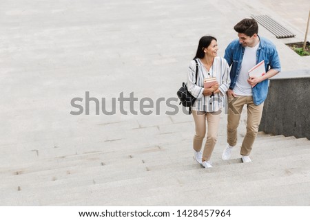 Photo of young happy cheerful amazing loving couple students outdoors outside walking by steps with books.