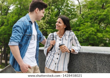 Image of nice couple man and woman with paper cup smiling and talking while standing on stairs outdoors