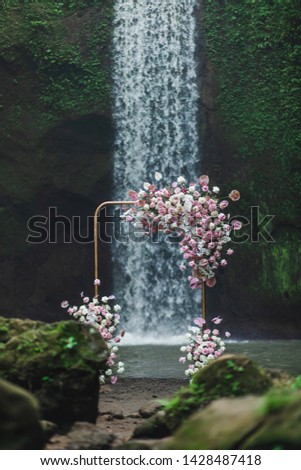Metal square wedding arch decorated with pink and coral colored flowers anthurium, orchids and roses. Modern and unusual style, wedding outdoors on Tibumana waterfall Bali.