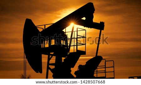 Silhouette of a oil pump jack in operation with beautiful orange sunset on the background.