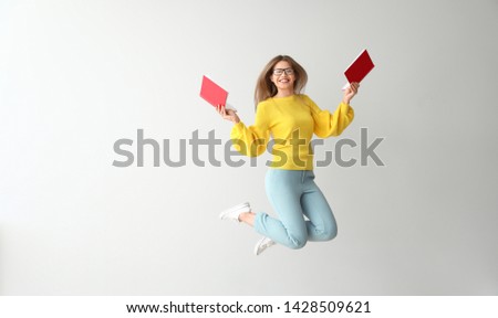Jumping young woman with books on light background