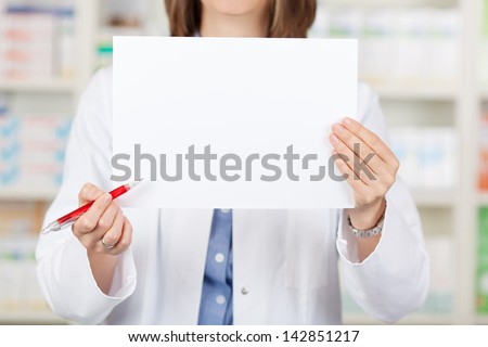 Midsection of female pharmacist holding pen while displaying blank paper in pharmacy