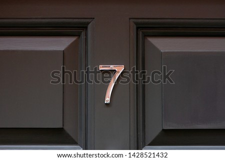 House number seven with the 7 in elegant silver on a black paneled wooden front door seen close up