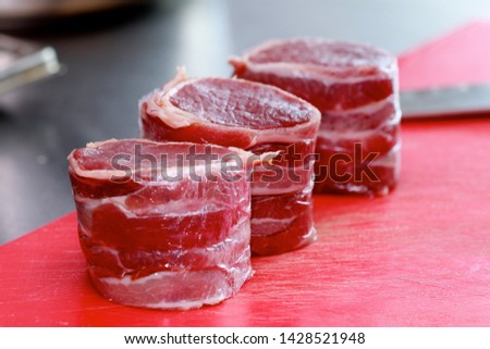 Raw fillet of  Hereford  Irish Beef Sirloin Steak wrapped in parma ham on a red meat board with knife in the background
